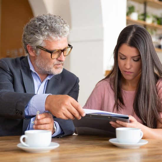 Mature legal advisor helping young customer to complete document form. Man and woman sitting at table and discussing papers. Expertise and paperwork concept